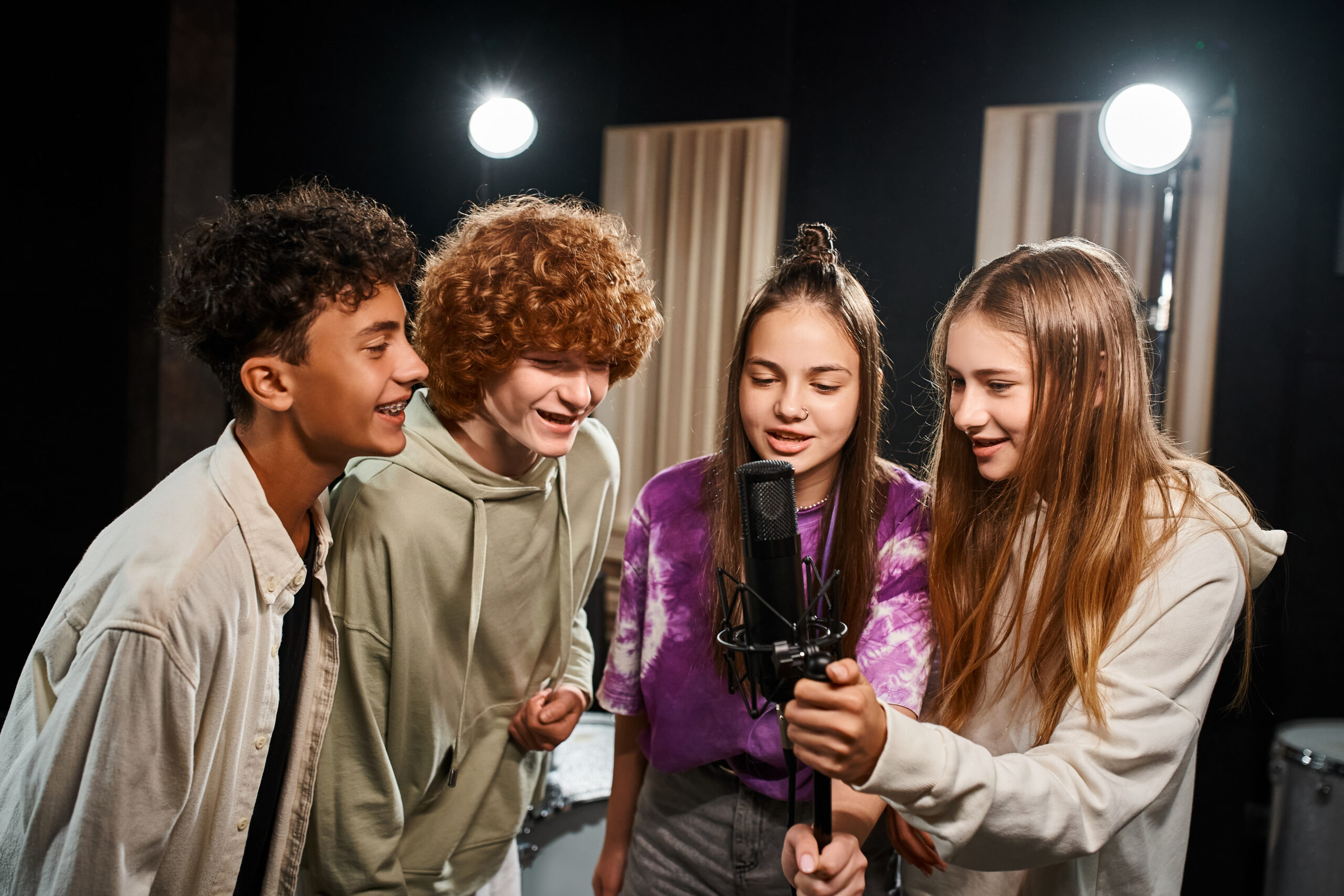 four joyous talented teenagers in casual outfits singing together while in studio, musical group